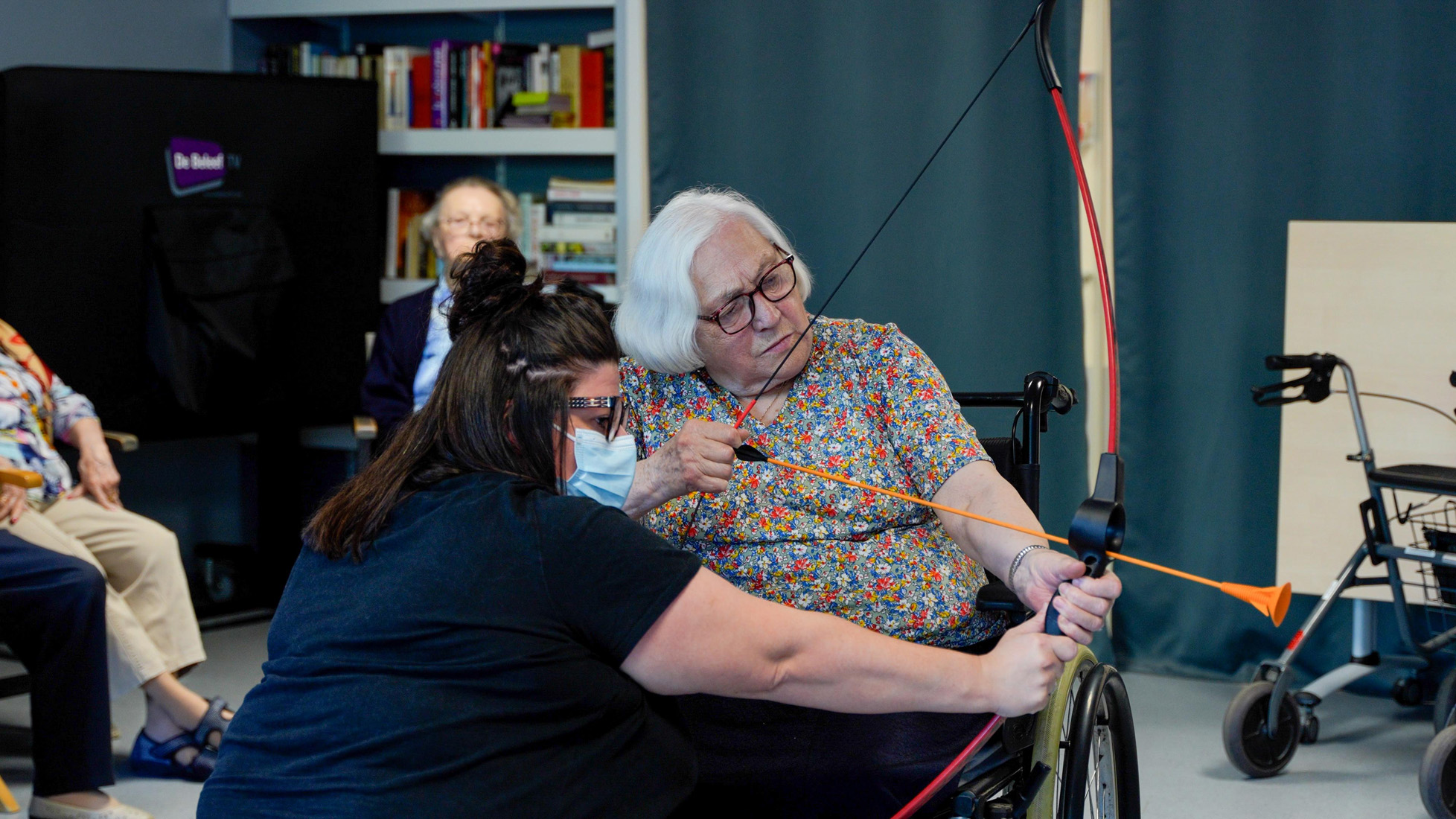 Senior woman practicing archery indoors with assistance
