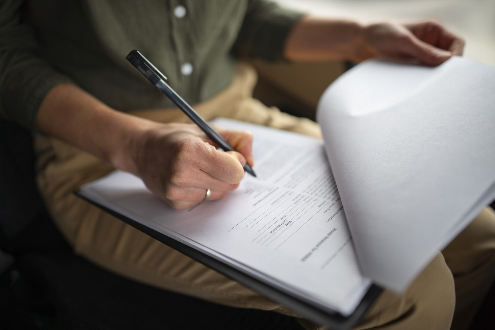 Person signing document on clipboard with pen