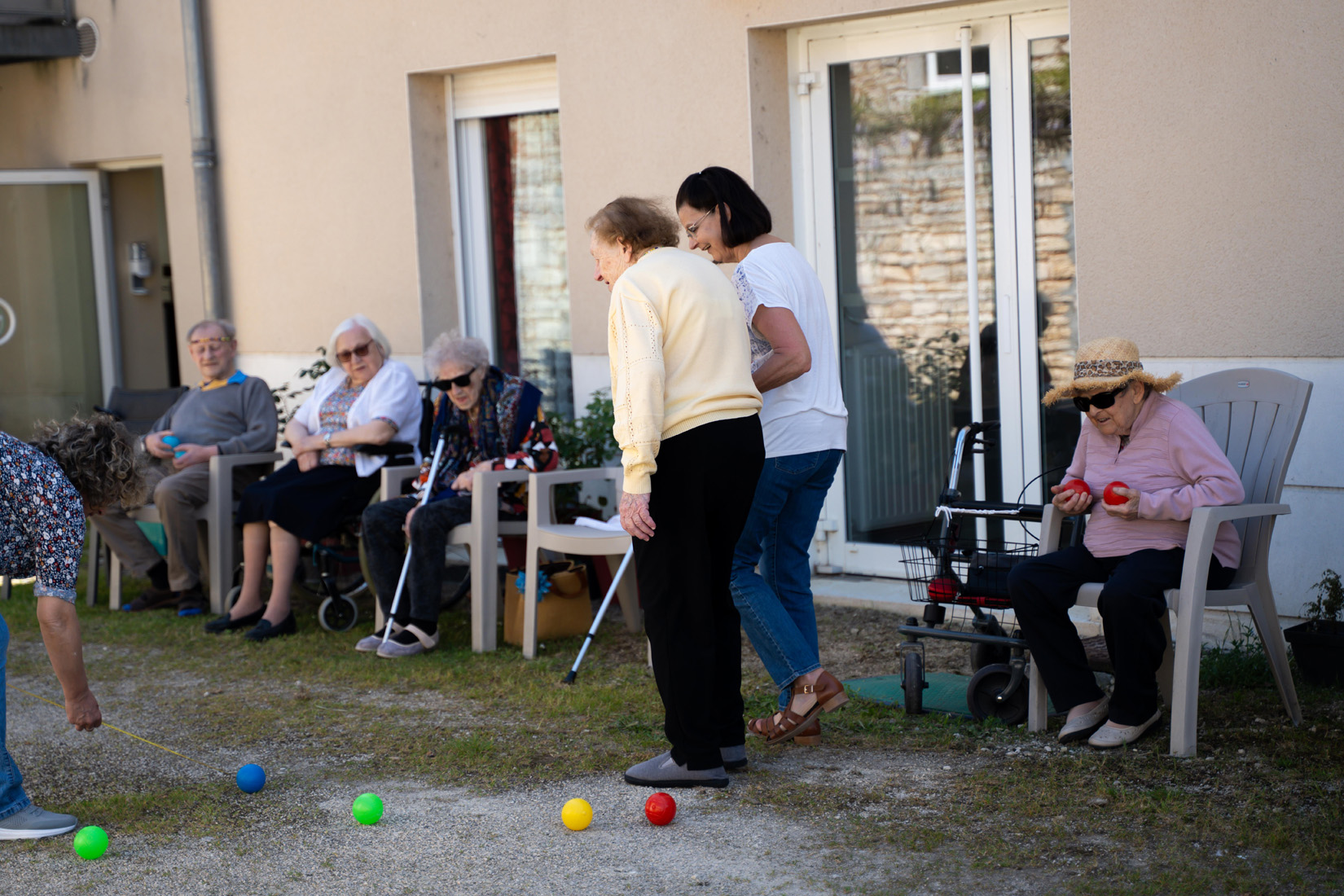 Seniors playing bocce outdoors with caregiver assistance