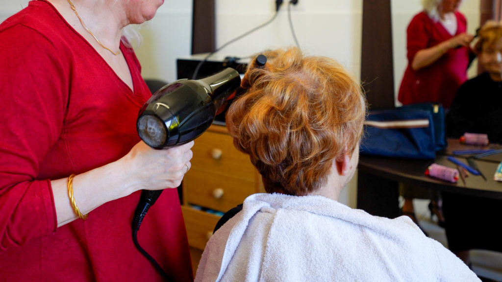 Hairdresser blow-drying elderly woman's short hair