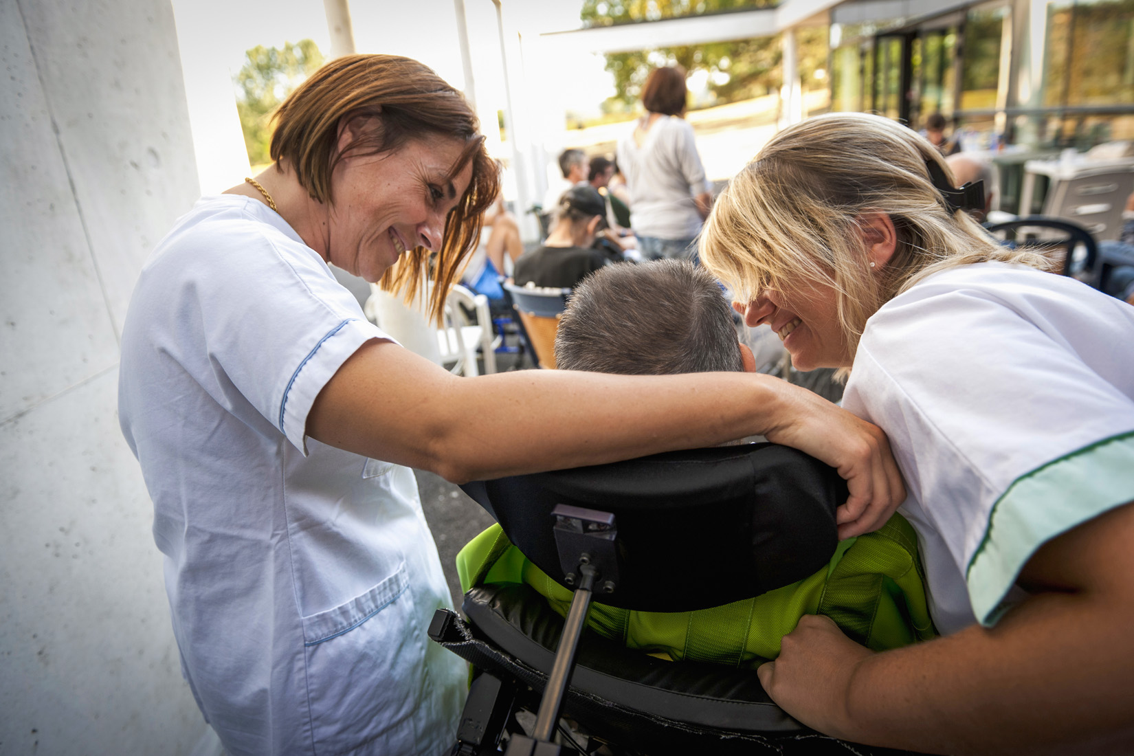 Caregivers smiling with child in wheelchair outdoors